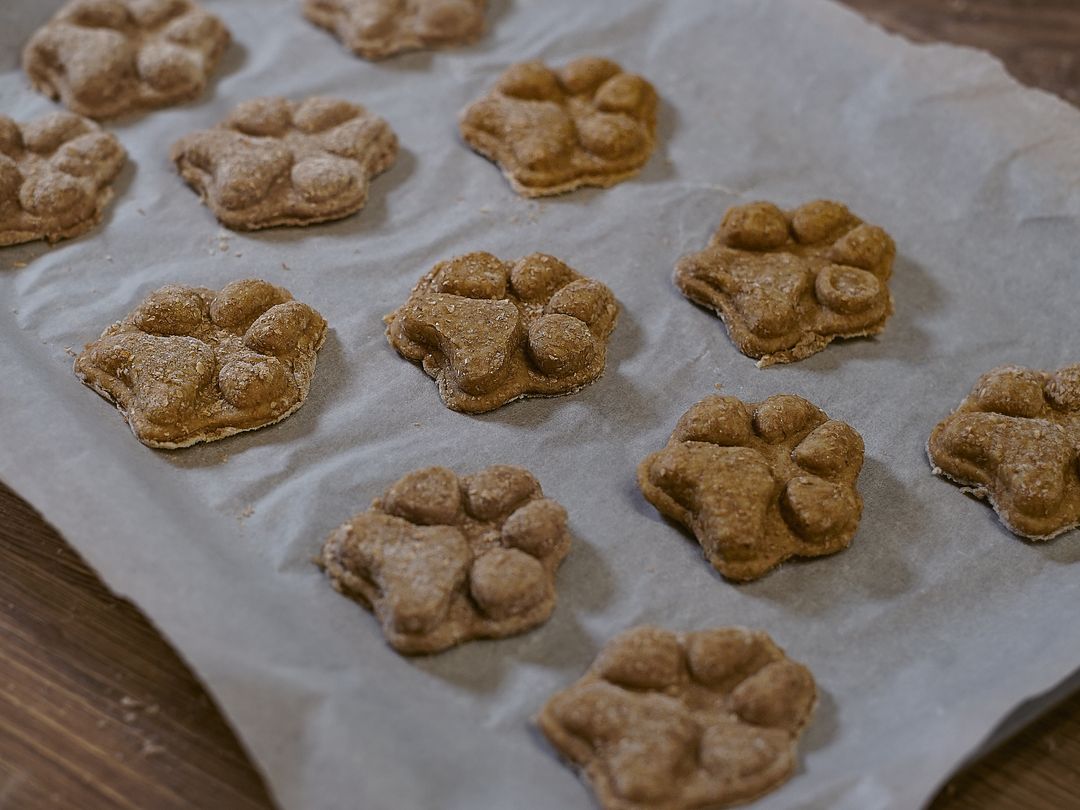 12 dog-friendly banana paw shaped cakes on a baking tray with baking parchment. 