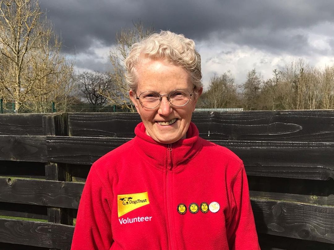 Isobel a older lady standing in a red volunteer fleece jacket outside.