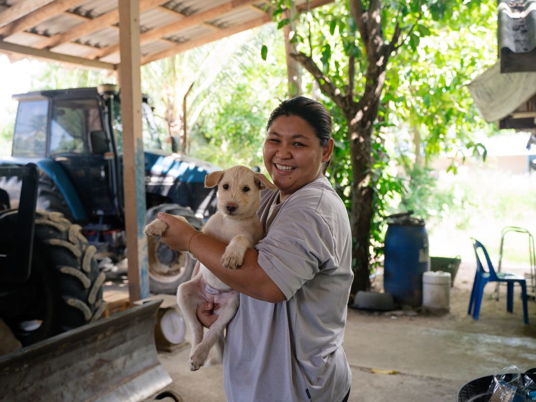 Woman holding a white haired stray puppy in her arms smiling in a yard near a blue tracker.