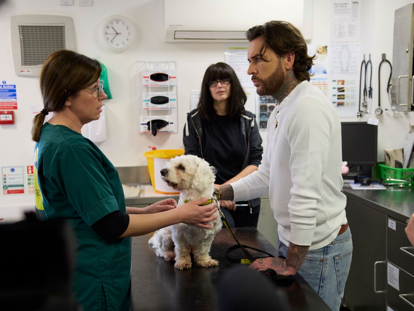 Pete Wicks behind the scenes at a Dogs Trust rehoming centre vetenary practice, with two members of staff and a small white Maltese-style dog