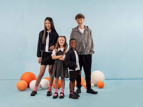 Group photo of two primary- and two secondary-school-aged children wearing Hush Puppies in front of a blue background with orange and white balloons.