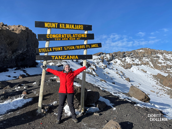 a lady standing in front of the famous mount Kilimanjaro plaque with her hands extended at her sides smiling