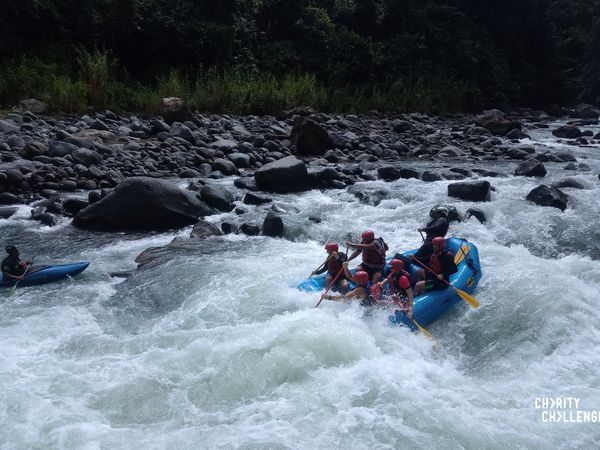 a group of people in a blue dinghy boat wearing red helmets paddling down some rapids on Pacuare River in Costa Rica
