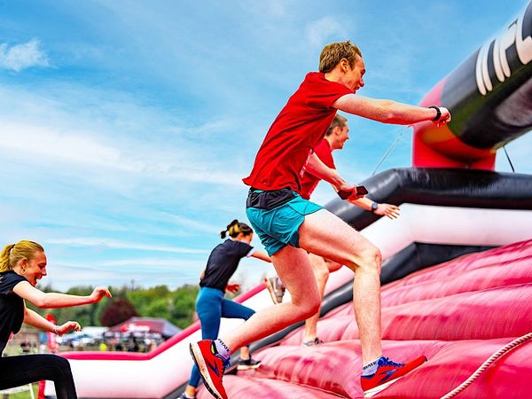 some people in gym clothes running up a large, red inflatable bridge