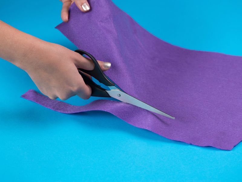 Close up of someone's hand holding scissors and cutting felt for a snuffle mat