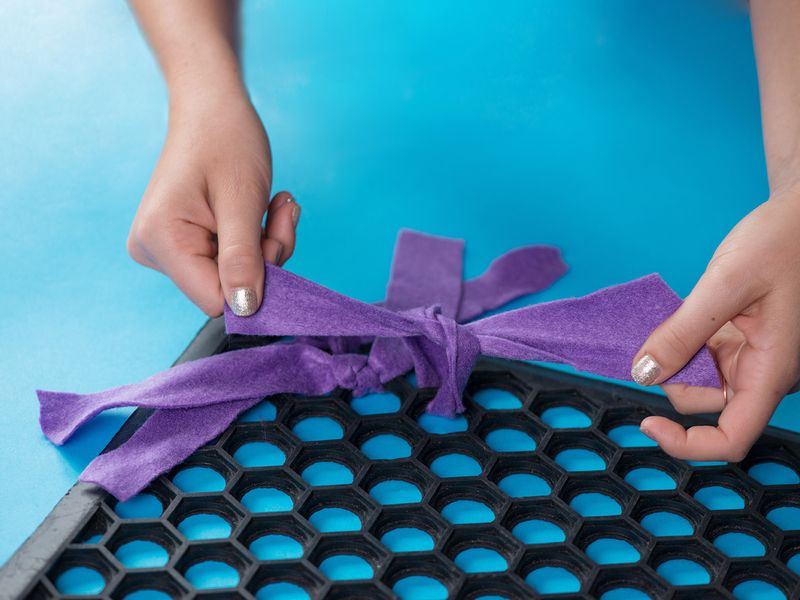 Close up of someone's hands tying felt into holes in a rubber mat