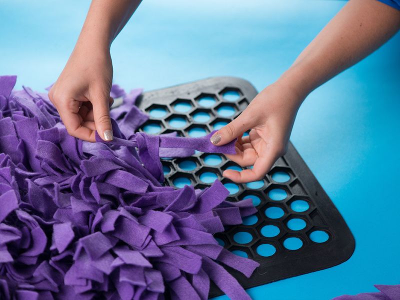 Close up of someone's hands tying fabric to rubber mat about two-thirds complete