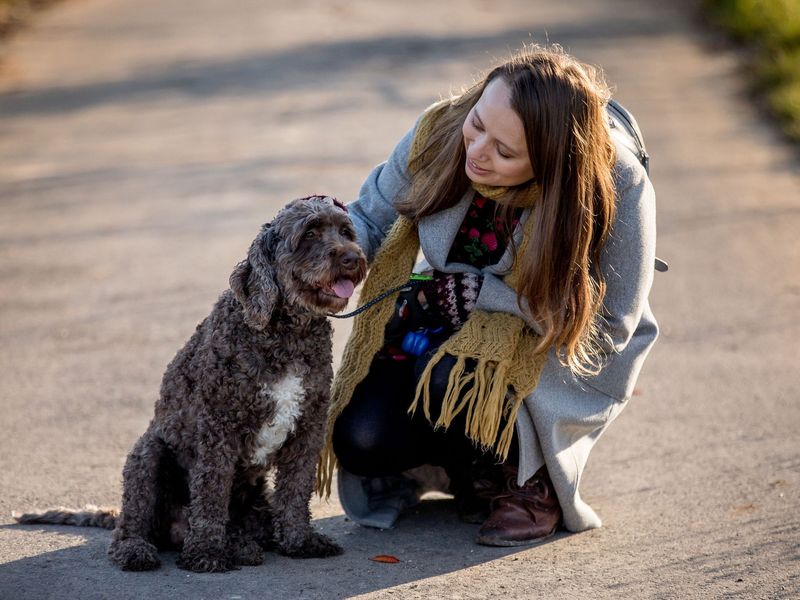 Dog owner Louisa outside on a path crouching down to pet her dog Matilda