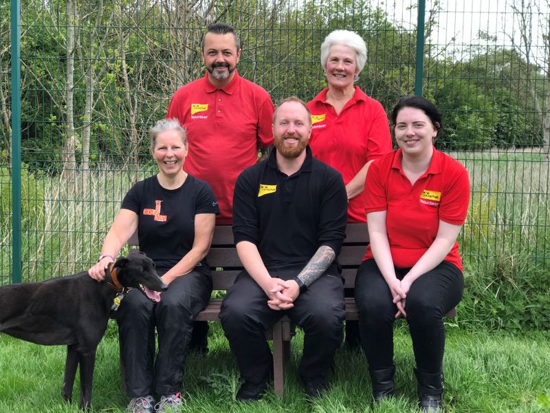 Dogs Trust West Calder volunteers and Volunteer Co-ordinator sitting with a black greyhound