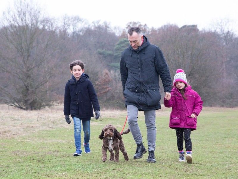 Adult male walking in a field with two children and a dog on a lead