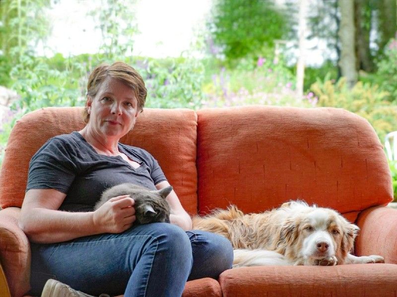Woman sitting on a sofa with a sleeping cat on her lap and a dog by her side