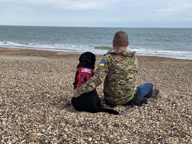 A veteran and his assistance dog hug on a beach