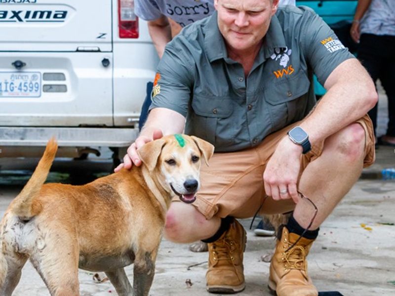 A vaccinated dog smiles with a Mission Rabies worker