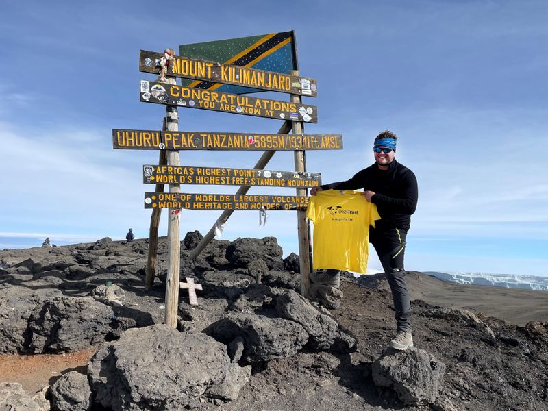 Fundraiser Simon Wilkes standing at the summit of Kilimanjaro mountain, holding a yellow dogs trust t-shirt.