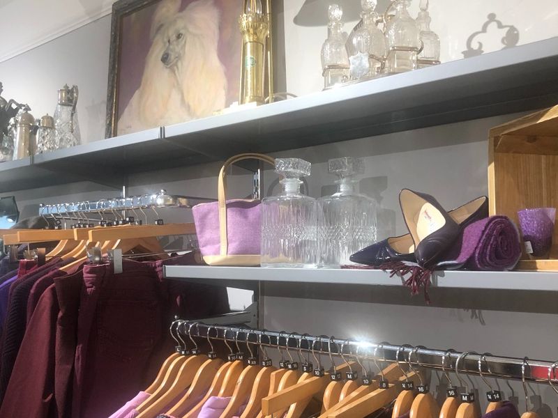 Image of a shop shelves with clothes hung up, bags, shoes and paintings.
