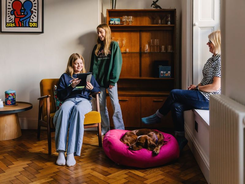 Family of three sitting in the living room with a brownish red Cocker Spaniel dog sitting in a pink dog bed. 