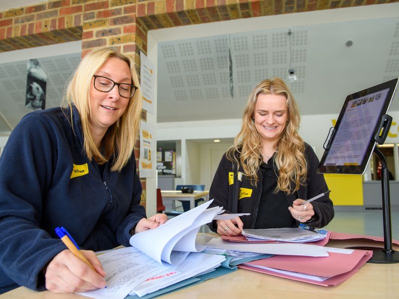 Basildon staff sitting together writing documents next to a computer.