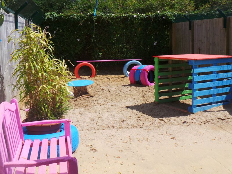 Shoreham Rehoming Centre outside in the sand play area with pink and blue painted wooden benches and sheds.