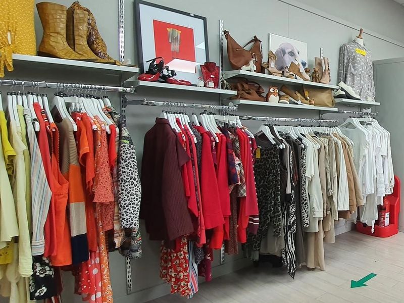 Ross on Wye charity shop with brightly coloured clothes on a rack.