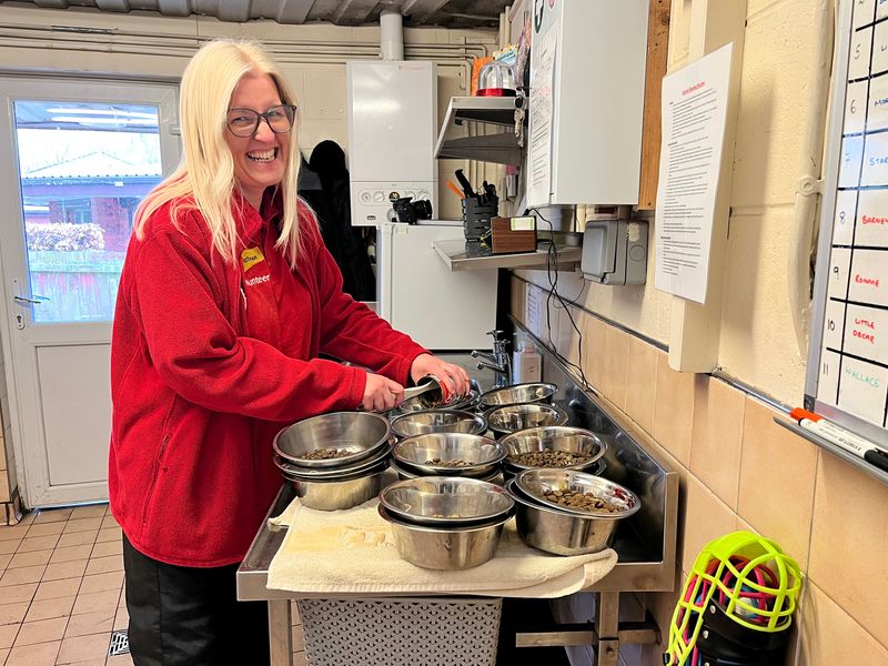 Alison one of our Volunteers wearing a red jacket prepping some food using lots of metal dog food bowls in a kitchen