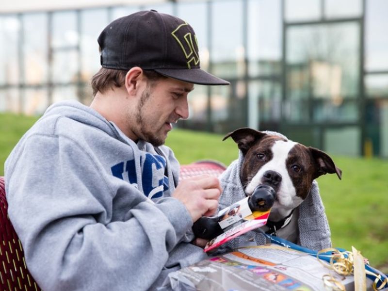 A dog owner and his Staffie who are experiencing homelessness open a Christmas gift.