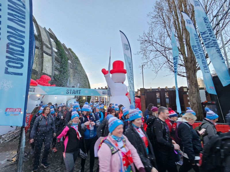 lots of people walking through a finishing line wearing blue wooly hats, with a large inflatable snowman in the background
