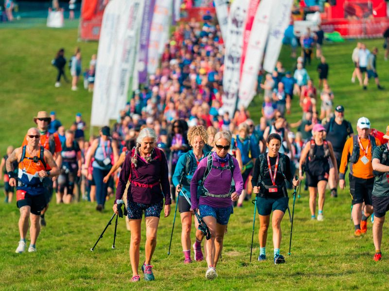 lots of people walking with hiking sticks in running gear on green grass, with the start line behind them