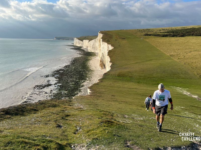 a line of people wearing white shirts, walking along a coastline