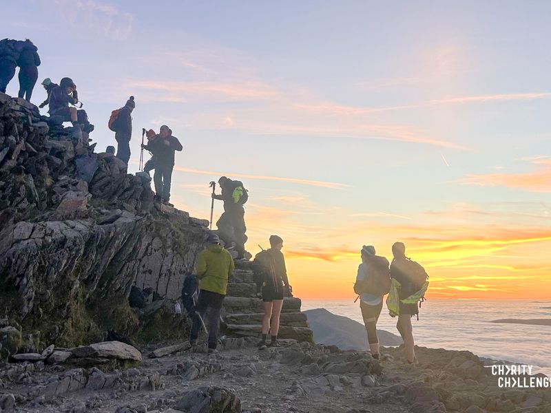 a line of people with hiking sticks walking up a rocky hill with steps in front of a bright orange sunset