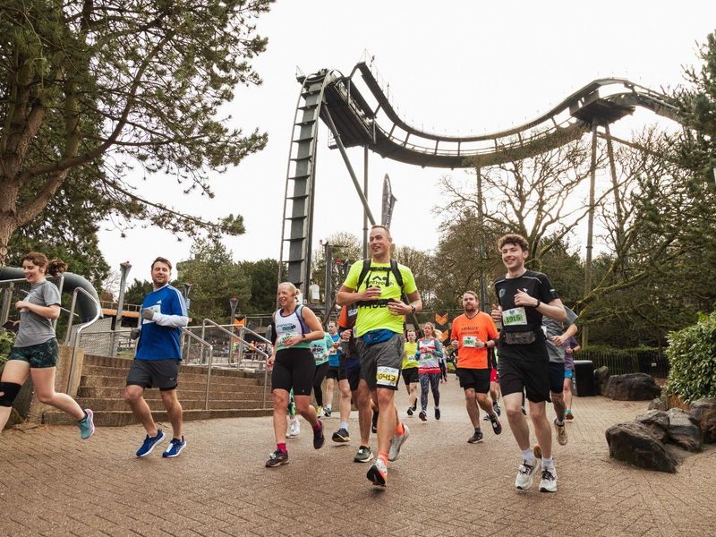 A group of people in running gear jogging past the oblivion ride in Alton Towers theme park