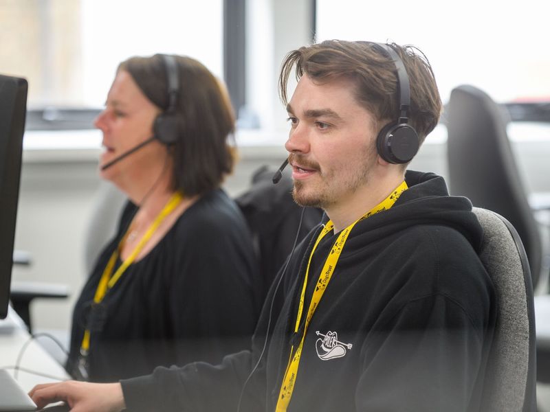 male staff member speaking to someone via telephone head set, sat at a computer at a desk