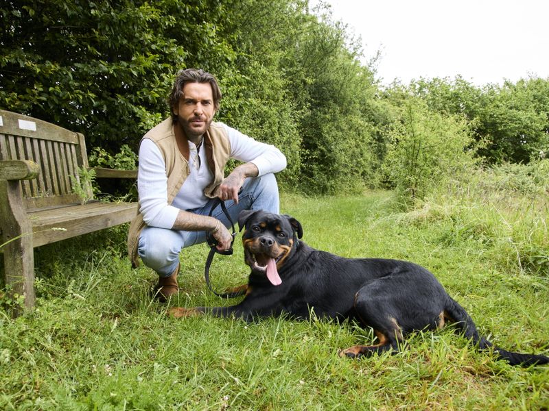 Pete wicks with Rodney a rottweiler adult dog posing near a bench