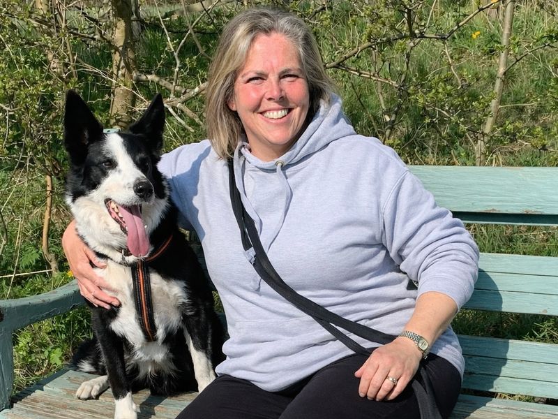 a black and white border collie sitting on a bench next to Julia his owner smiling